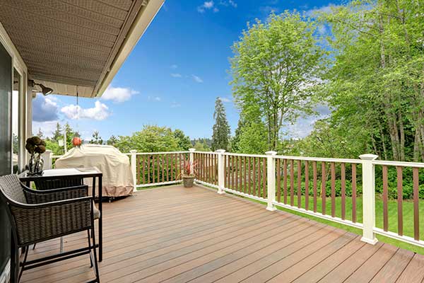 Wooden deck area with some furniture and railings overlooking trees in the backyard of a home