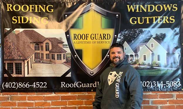 Owner, Dion Hancock, in front of an Roof Guard advertisement banner